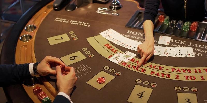 Croupier donna del blackjack che indica, con il dito della mano sinistra, una scritta al giocatore seduto di fronte