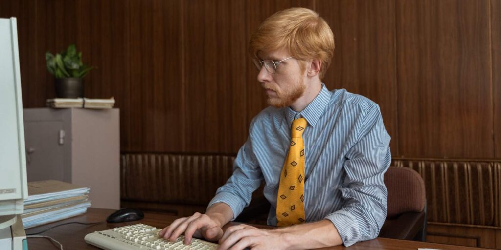 Uomo d’affari con i capelli rossi che scrive con la tastiera del computer desktop negli anni ’90